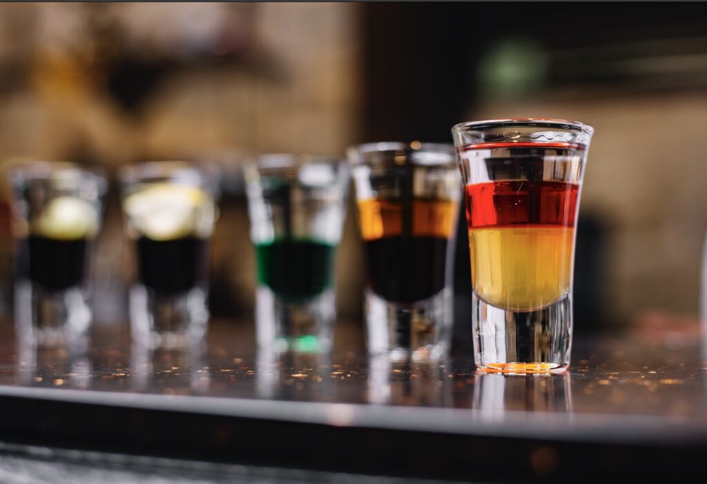 There are 5 different colored small shots on the bar counter.