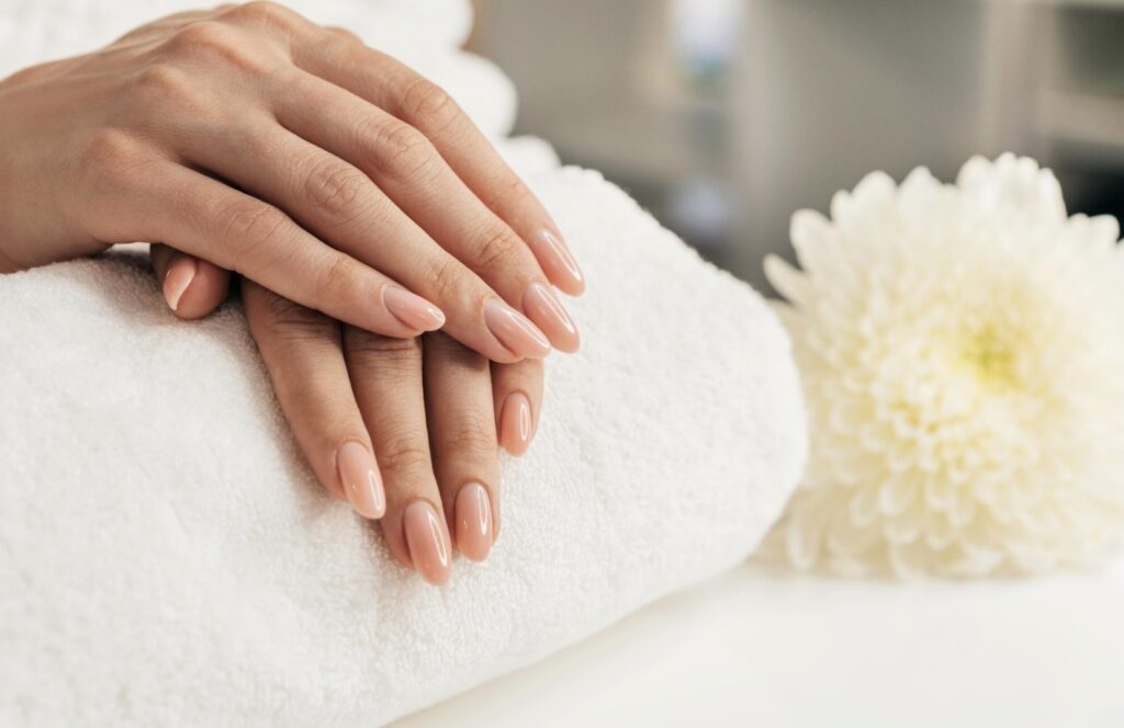 Two well-groomed hands of a girl with pink nails lie on a towel roll. White flowers lie nearby
