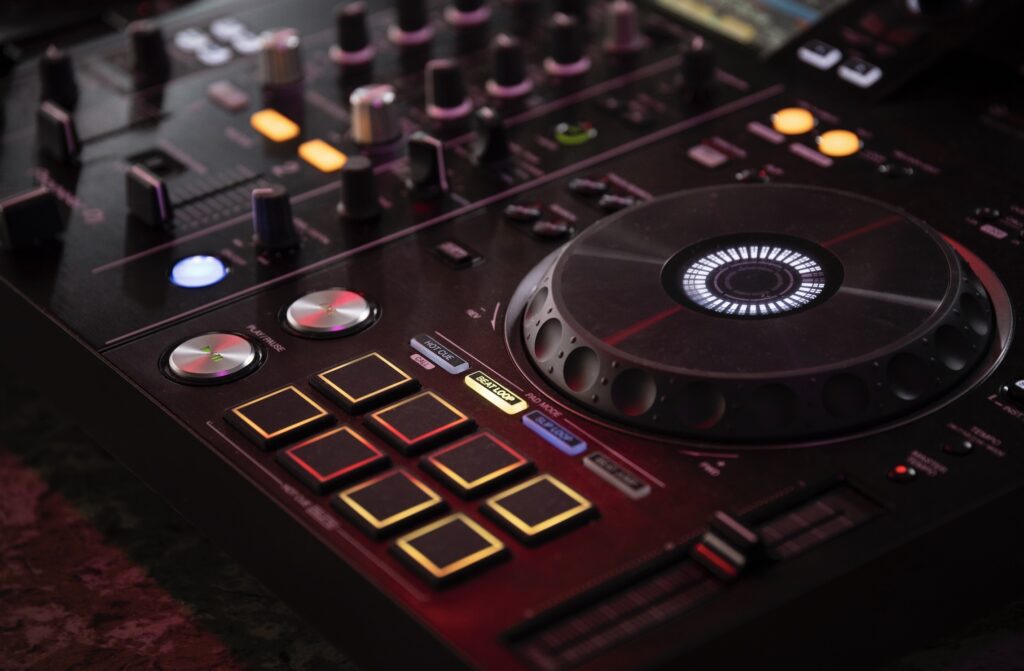 Close-up of a DJ controller with illuminated pads, glowing buttons, and a jog wheel displaying light patterns in a dimly lit atmosphere.