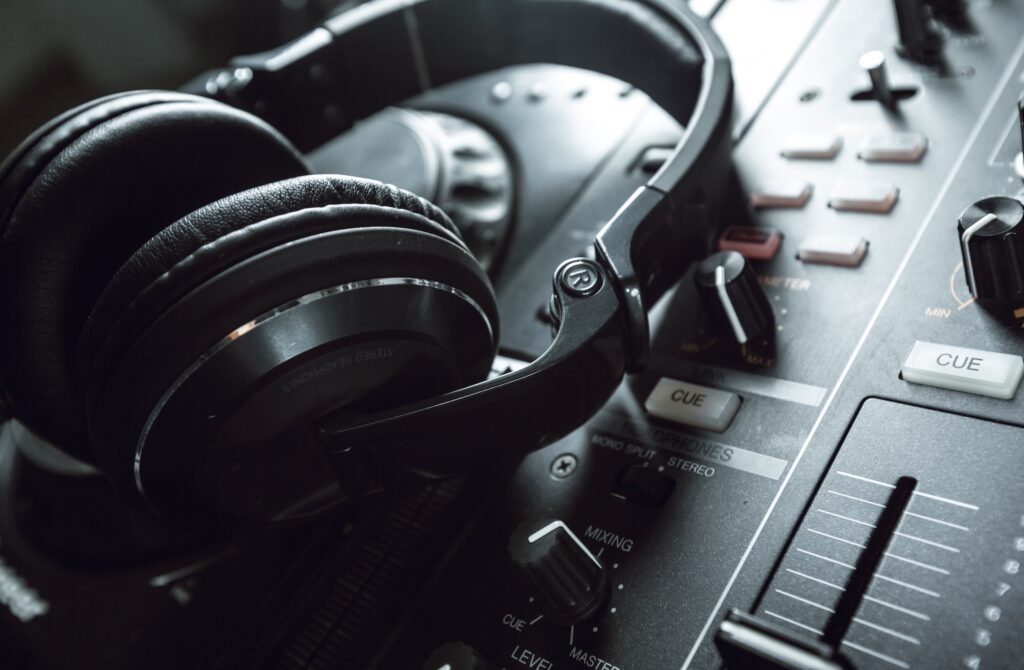 Black headphones rest on a DJ mixer with detailed controls, knobs, and faders, highlighting the professional audio setup in soft lighting.
