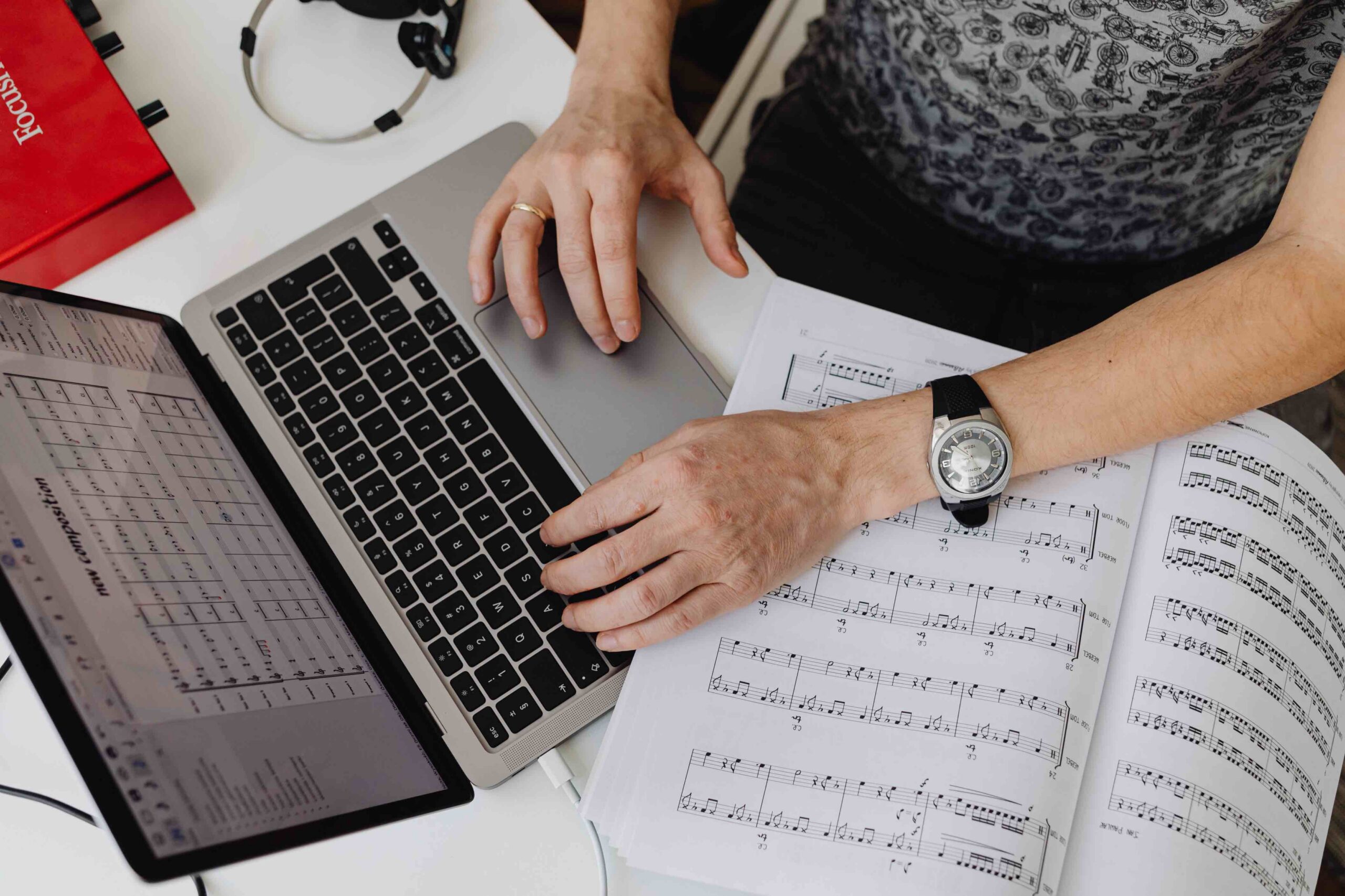 An overhead shot of a musician typing on a laptop next to a notebook filled with sheet music.