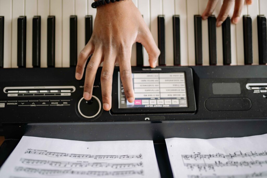 An overhead shot of a person's hands on a digital piano keyboard, with one hand interacting with the central digital preset display screen.