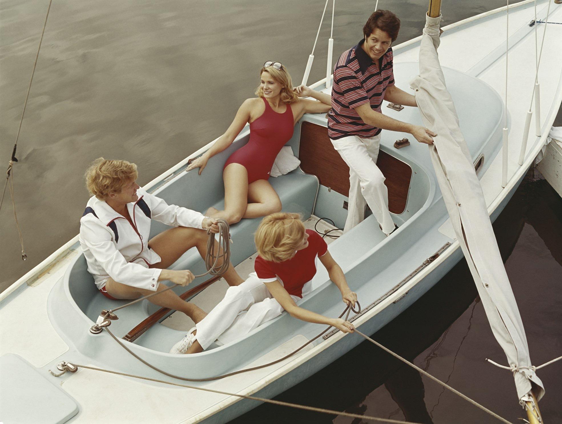 Four people in retro 1970s nautical attire enjoying a sunny day on a vintage sailboat, perfectly capturing the yacht rock lifestyle aesthetic.